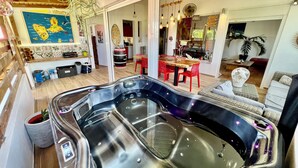 Een moderne woonkamer met een grote hottub, houten vloeren en een eethoek met rode stoelen.