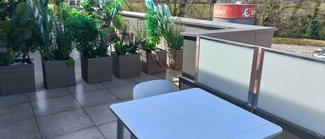 A terrace with a table and chairs, potted plants, and a view of a hilly landscape.
