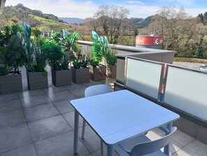 A terrace with a table and chairs, potted plants, and a view of a hilly landscape. - B&B Hotel Castro Urdiales (Castro Urdiales)