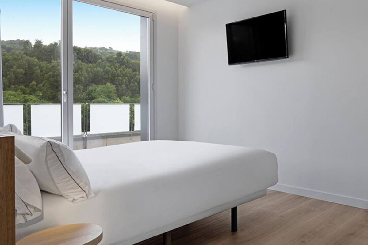 A bedroom with a bed, a TV mounted on the wall, a chair, and a view of a lake.