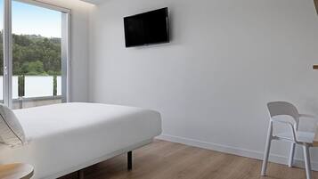 A bedroom with a bed, a TV mounted on the wall, a chair, and a view of a lake.