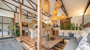 Una sala moderna con una mesa de centro de madera, un sofá con cojines estampados y un comedor con una mesa y sillas blancas.