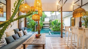 Een moderne woonkamer met een bank, een houten salontafel en hangende rieten lampen.