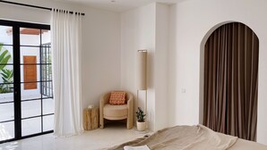 Une chambre moderne avec une grande fenêtre, un lit avec une couverture, une chaise, une lampe sur pied et une vue sur l’extérieur.