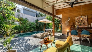 A modern outdoor patio with a pool, lounge chairs, and a dining area with a wooden ceiling and artwork. - Splendid Villa Shakti Canggu Boho chic 3bd & Pool (Canggu)