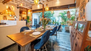 A dining area with wooden tables and blue chairs, surrounded by plants and artwork. - Splendid Villa Shakti Canggu Boho chic 3bd & Pool (Canggu)