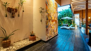A hallway with a decorative wall, potted plants, a mural, and a wooden floor. - Splendid Villa Shakti Canggu Boho chic 3bd & Pool (Canggu)