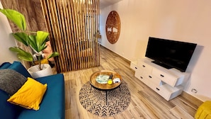 A modern living room with a blue sofa, a wooden coffee table, a television on a white stand, and a decorative wall piece.
