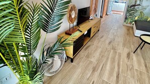 En moderne stue med et træ-tv-bord, en stor stueplante og en ventilator.