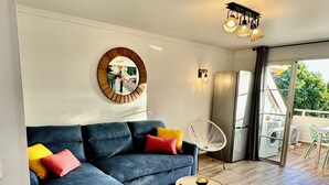 Una sala de estar moderna con un sofá azul, cojines coloridos, una obra de arte redonda en la pared, una silla blanca y una mesa de centro de madera.