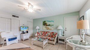Ein Wohnzimmer mit Fernseher, einer Couch, einem Couchtisch und einem Deckenventilator.