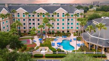 A hotel with a swimming pool, palm trees, and a view of the cityscape.