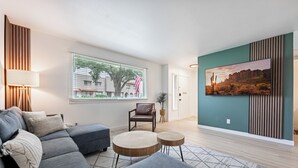 Ein modernes Wohnzimmer mit einem Ecksofa, einem kleinen runden Tisch und einem an der Wand befestigten Fernseher.