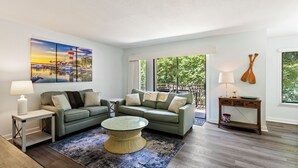 A modern living room with a green sofa, a glass coffee table, and a painting of a sunset over a marina. - Sea Pines -Spacious & Renovated, Heart of Harbour Town, Pet Friendly (Hilton Head Island)