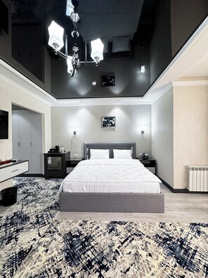 A modern bedroom with a large bed, bedside tables, a desk, and a patterned rug. - De Villa Hotel (Samarkand)