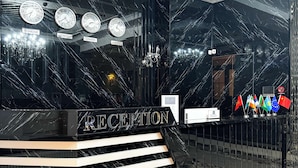 A reception area with a marble wall, clocks, and a chandelier. - De Villa Hotel (Samarkand)