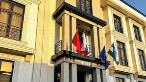 A hotel facade with classical architecture, featuring a prominent entrance with steps leading up to the door, and flags of China, France, and the European Union displayed. - De Villa Hotel (Samarkand)