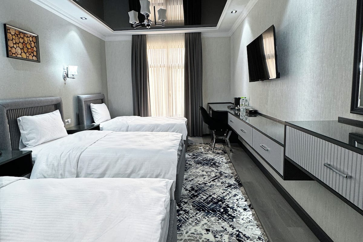 A hotel room with two beds, a desk, a TV, and a large window with curtains.