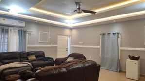 Un salon avec un canapé en cuir marron foncé, une table d’appoint blanche et un ventilateur de plafond.