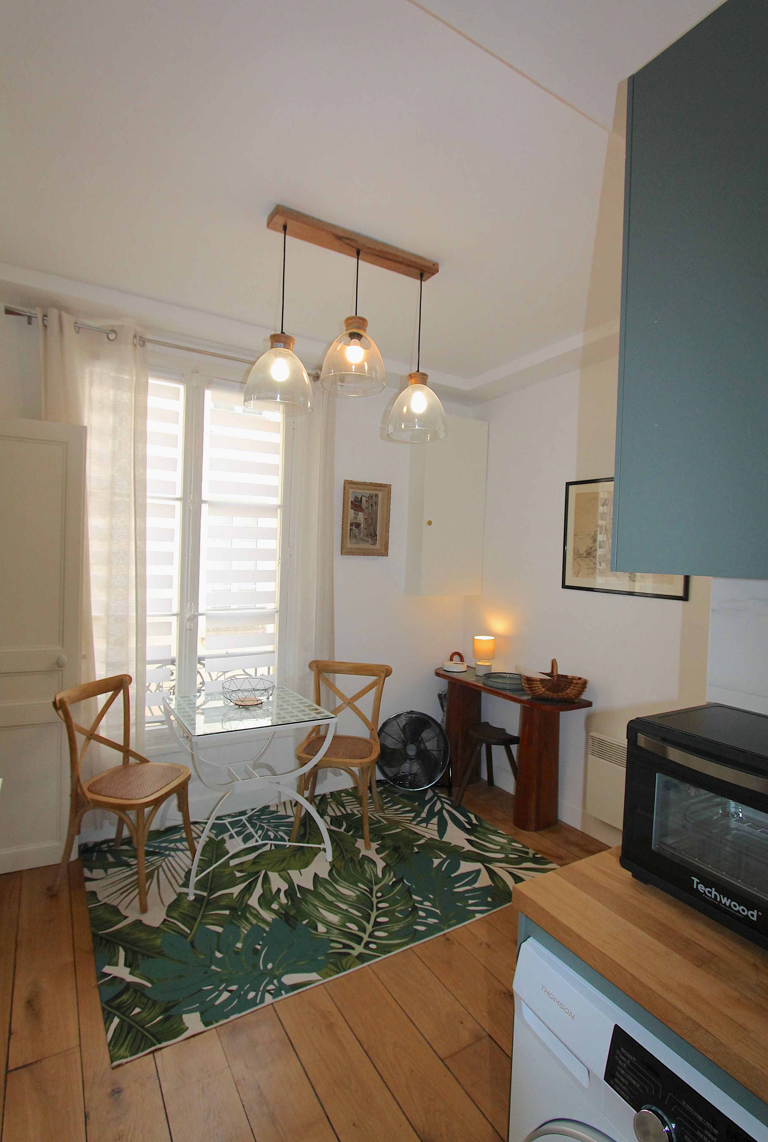 A compact kitchen with a dining table, chairs, a fan, a microwave, and pendant lighting.