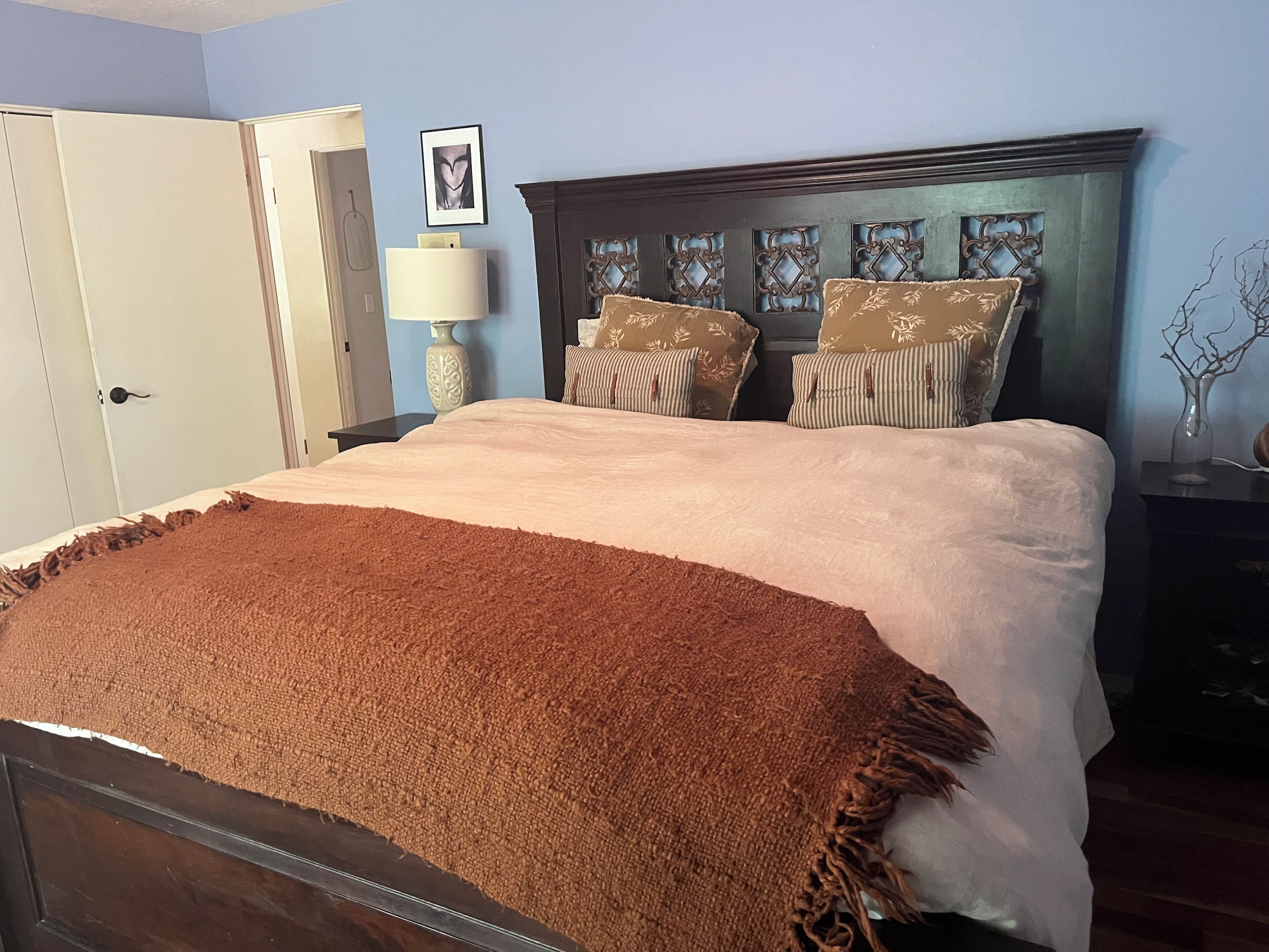 Un dormitorio con cama, mesita de noche, lámpara y puerta.