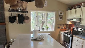 A kitchen with a central island, white cabinetry, a stove, and a window with a view of trees. - Beautiful family home in the Upper Rattlesnake (Missoula)
