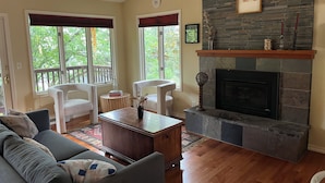 A living room with a fireplace, a sofa, two chairs, a coffee table, and large windows with blinds. - Beautiful family home in the Upper Rattlesnake (Missoula)