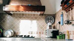A kitchen with a brick chimney, tiled backsplash, wooden cabinets, and a countertop with various kitchen items. - Amber apartment  (Essaouira)