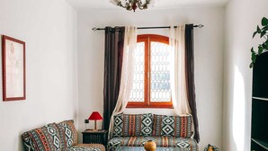 A cozy living room with a patterned sofa, a small table, and a window with curtains. - Amber apartment  (Essaouira)