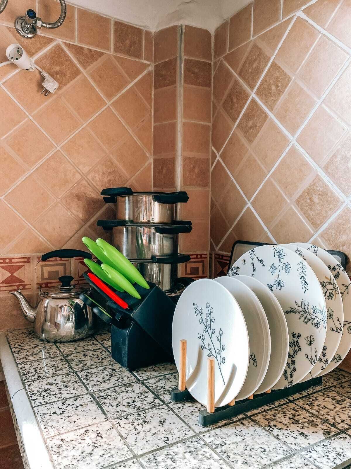 A kitchen with a tiled backsplash, a kettle, pots, and a rack of plates.