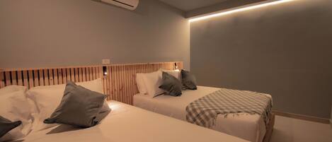 Ein Hotelzimmer mit zwei Betten, einem Holz-Kopfteil, einer karierten Decke und einer Klimaanlage.