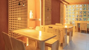 Un intérieur en bois avec des tables et des chaises, un luminaire fixé au mur et une cloison décorative en bois.