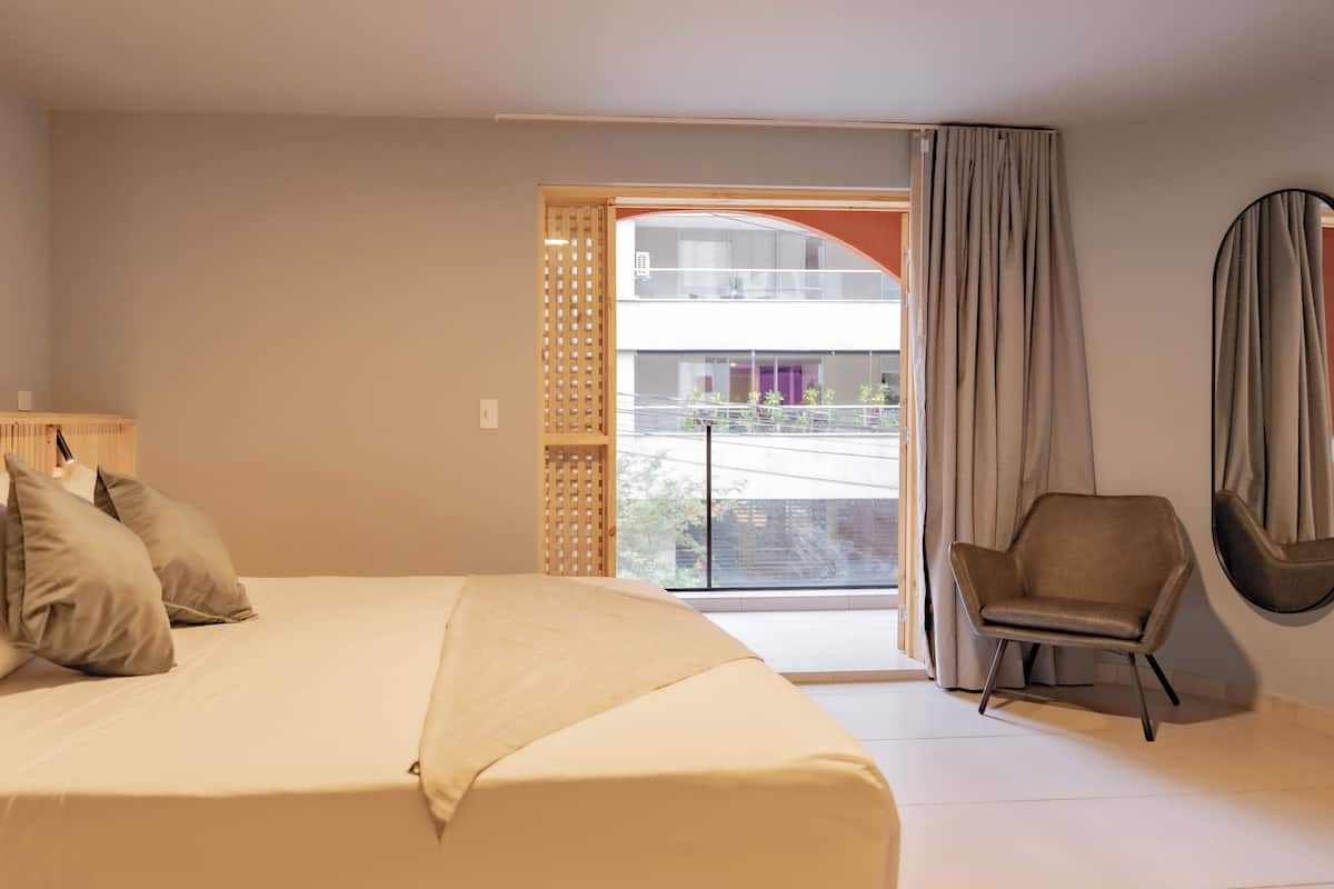 Habitación de hotel con cama, una silla, ventana con cortinas y vistas al exterior.