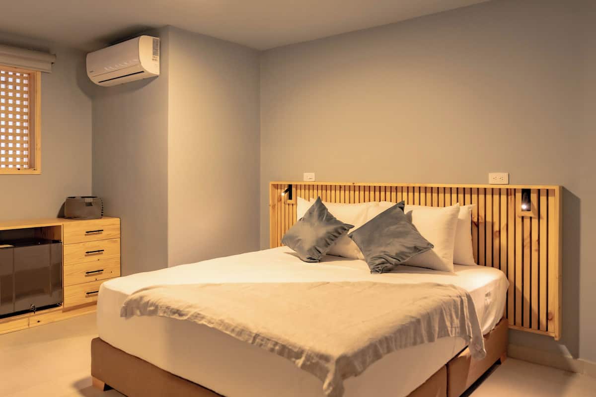 Un dormitorio con una cama, cabecera de madera, mesitas de noche y un equipo de aire acondicionado.