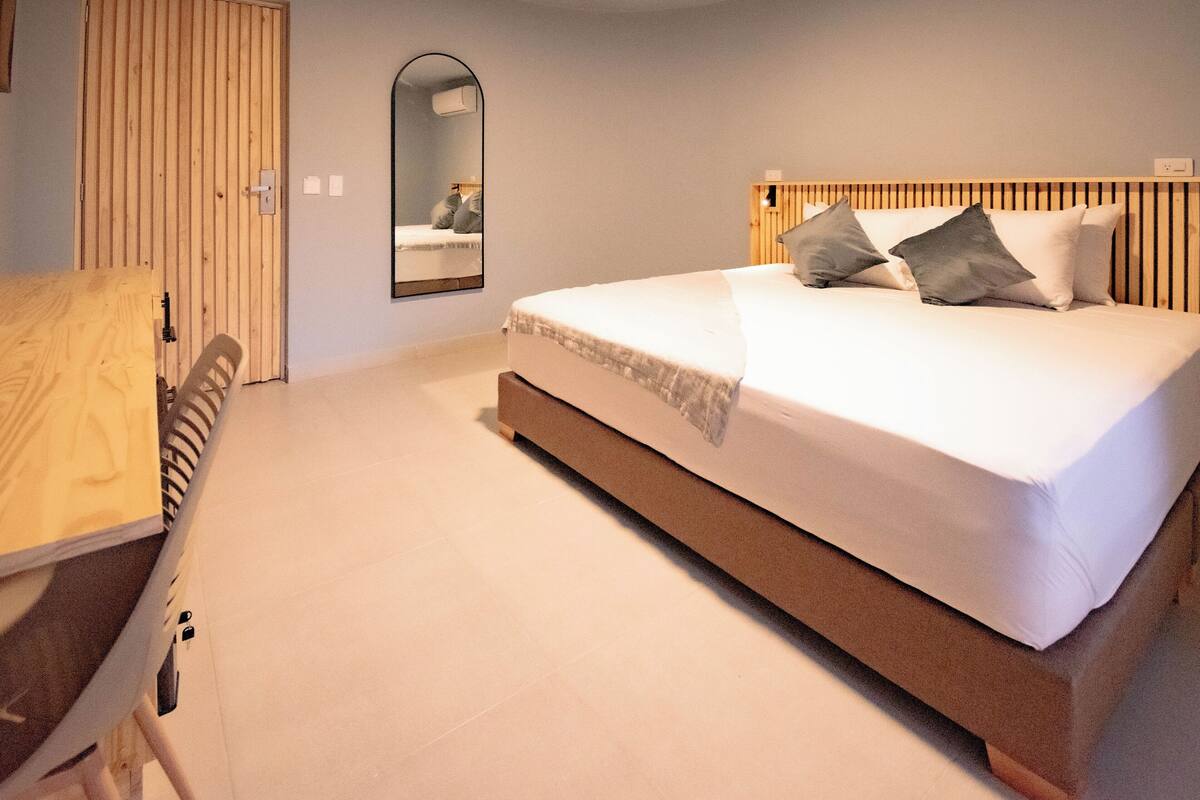 Un dormitorio con una cama, cabecera de madera, un espejo, armario y escritorio.