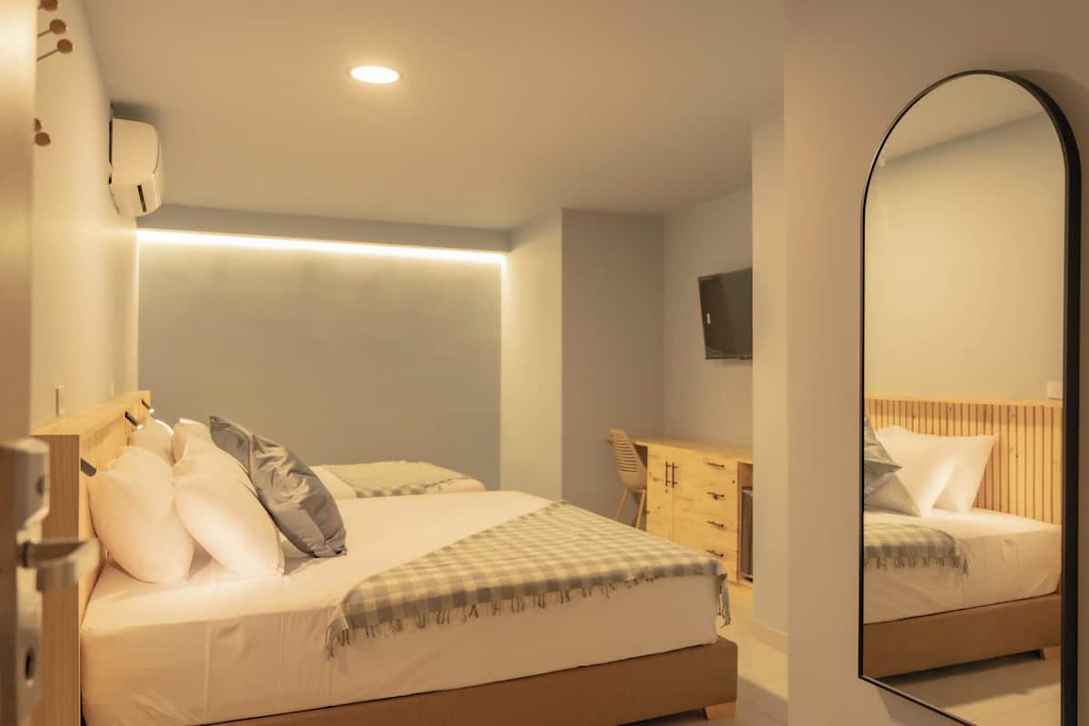 Un dormitorio con cama, mesita de noche, espejo y televisor de pared.