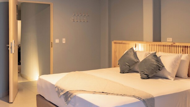 Une chambre moderne avec un grand lit, une tête de lit en bois et un couloir menant à une autre pièce.