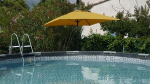 En pool med klart vatten och en kant av kakel, ett gult parasoll och en stege.