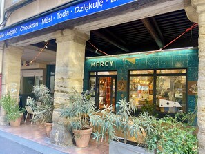 A storefront with a sign that reads 'Mercy' and a variety of potted plants in front.