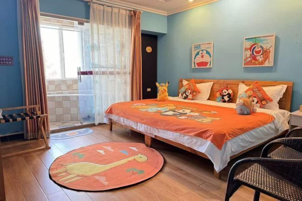 A bedroom with a bed, a window with curtains, a wooden floor, and a round rug.