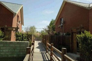 Un sendero conduce a un edificio de ladrillo con cerca de madera y un puente de madera.