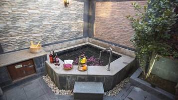 Relax in a serene outdoor spa area with a central hot tub, surrounded by a stone wall and a wooden fence.