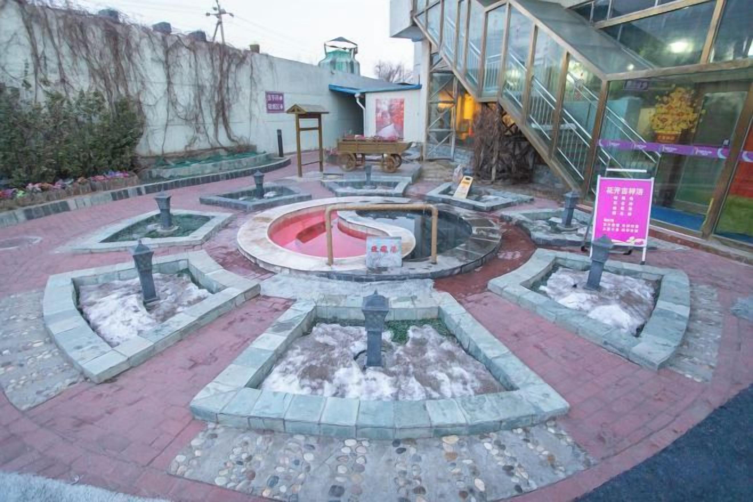 A courtyard with a central fountain, surrounded by stone planters and a building entrance.