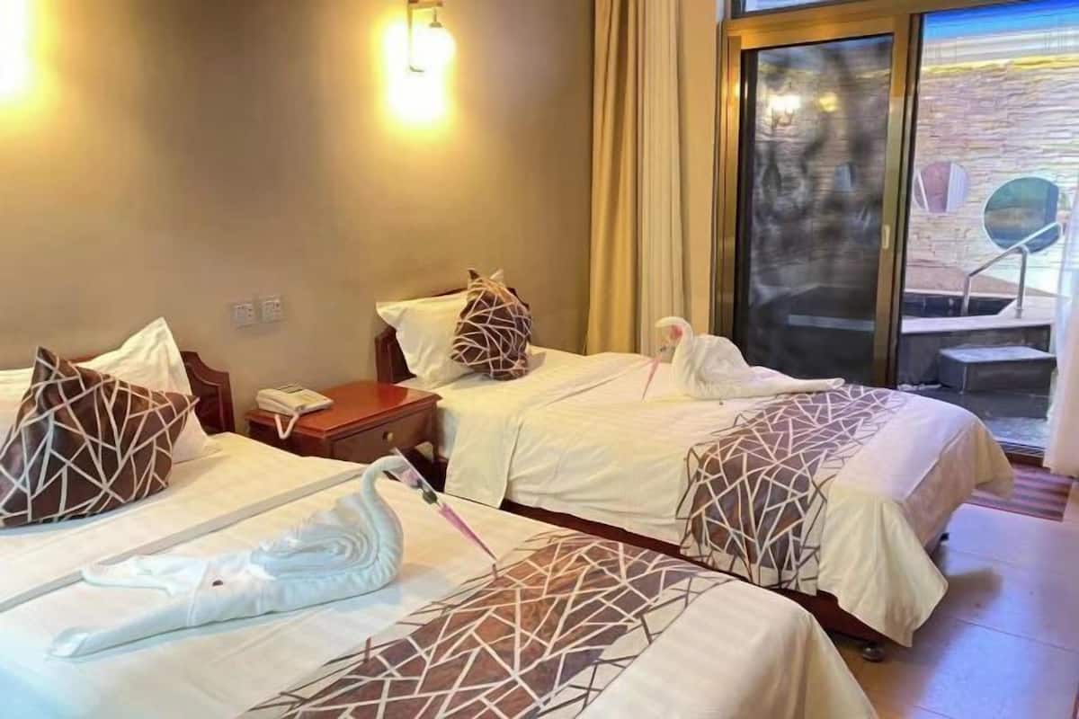A hotel room with two beds, each with geometric-patterned bedding, a bedside table with a phone, and a view through a glass door.