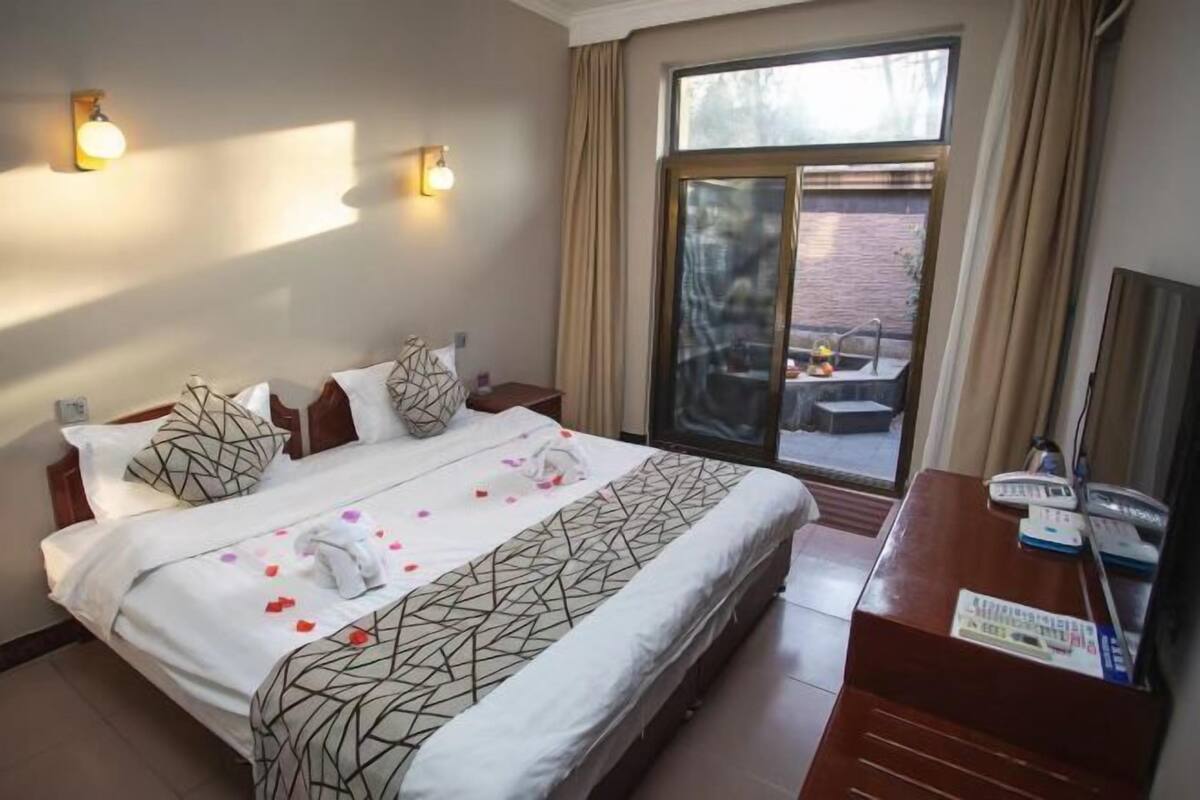 A hotel room with a bed, a desk with a telephone, and a window with a view of the outside.