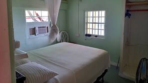 A room with a bed, a window with bars, a standing fan, and a ceiling fan. - Rainbow Beach - Apartment with an amazing seaview (Calibishie)