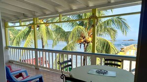A balcony with a view of palm trees and the sea. There is a table with a green tablecloth and two chairs. - Rainbow Beach - Apartment with an amazing seaview (Calibishie)
