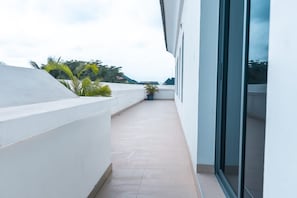 A narrow balcony with a tiled floor, potted plants, and a view of the sky and distant trees. - Bluerock Residences (Lekki)