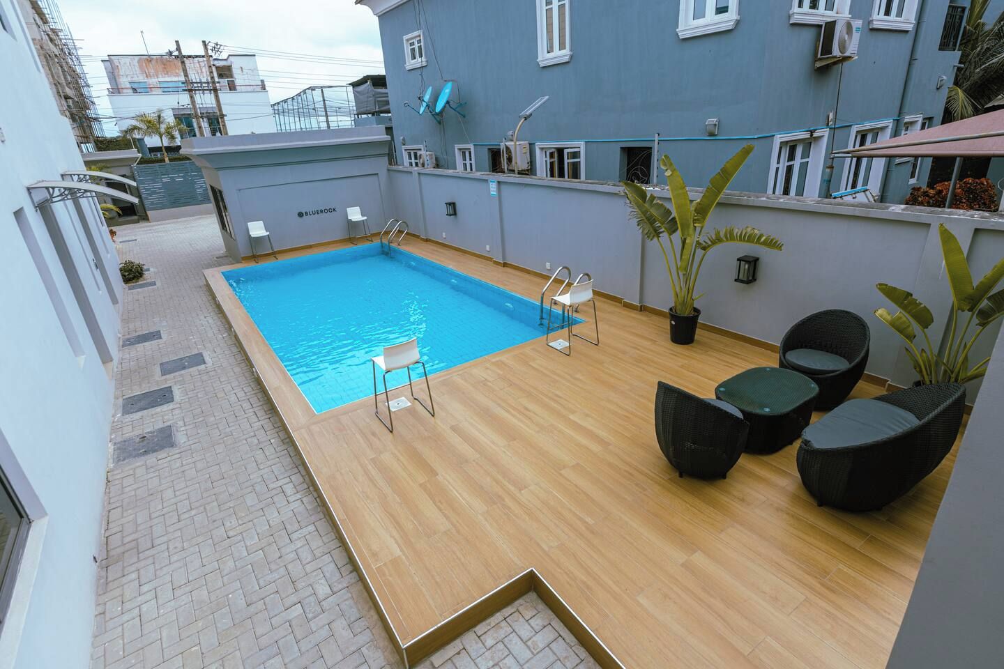 Une piscine sur le toit, avec une terrasse en bois, quelques chaises et des plantes en pot.