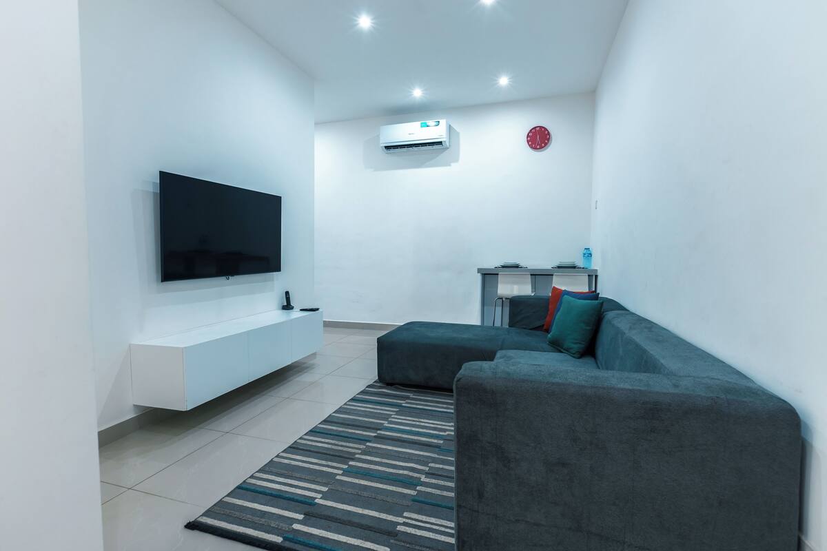Un salon moderne doté d’un téléviseur à écran plat, d’un meuble de rangement blanc, d’un canapé gris et d’un tapis à motifs.